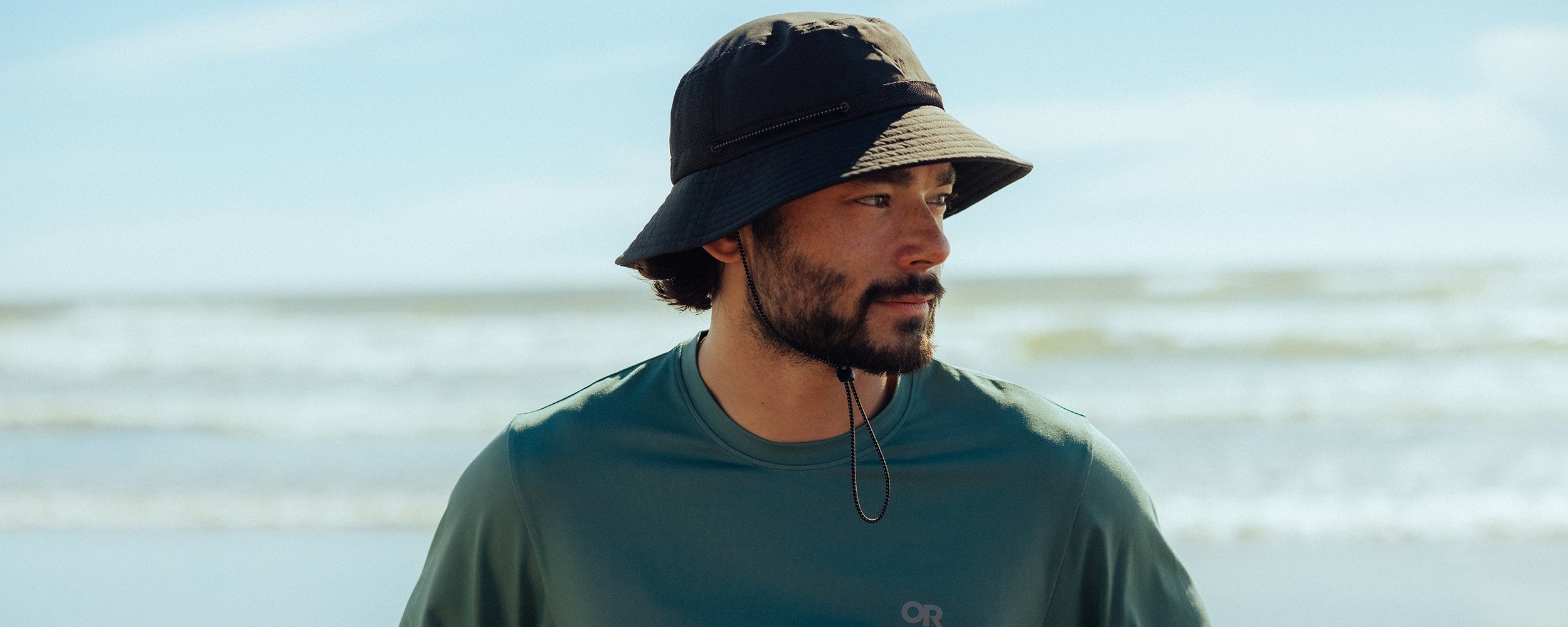 Man looks at the ocean view around him while wearing Outdoor Research ActiveIce Spectrum Sun Long Sleeve in Neptune.
