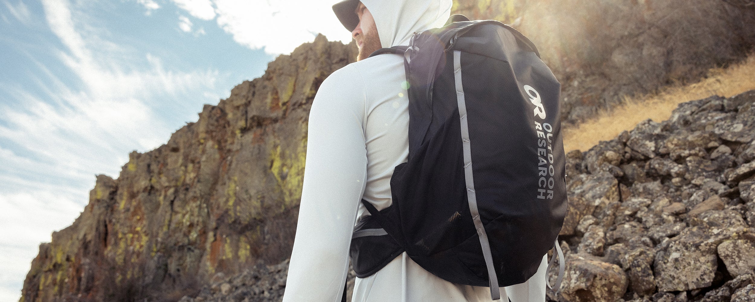 A man wears the Adrenaline Day Pack 30L in Black while hiking on a sunny day.