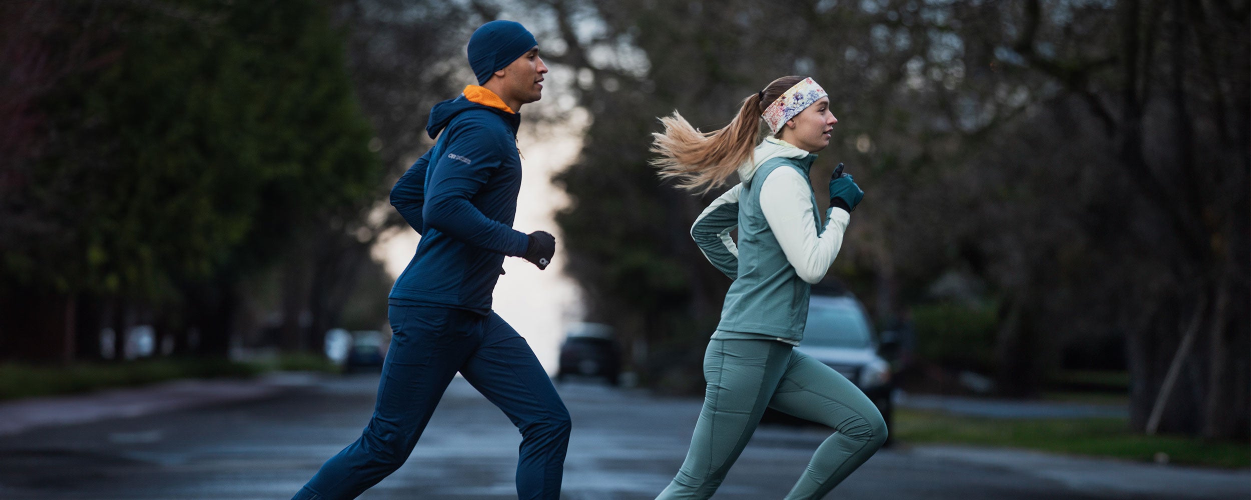 Two runners jog across the crosswalk wearing Outdoor Research Deviator styles.. 