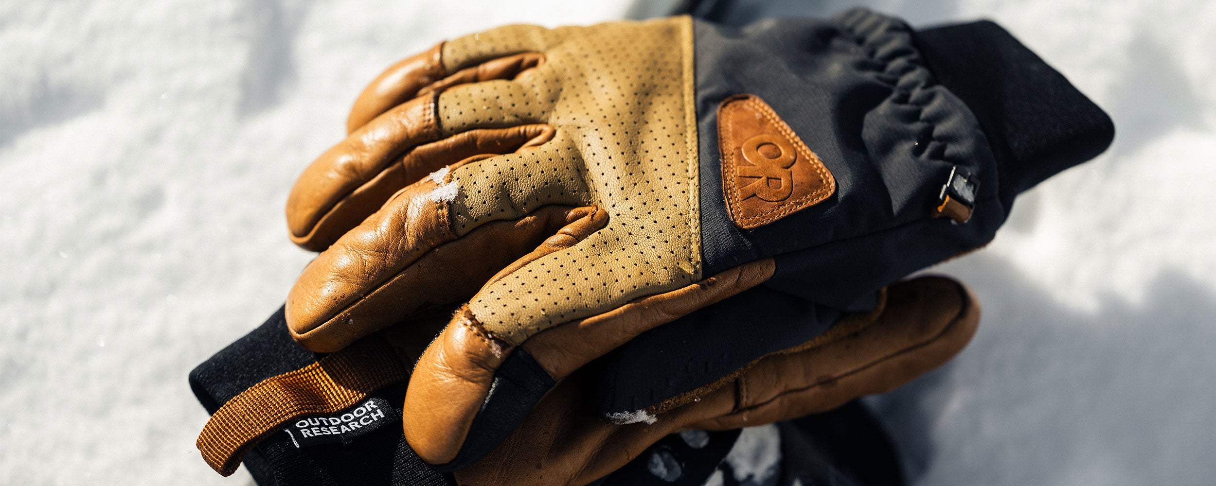 A pair of Outdoor Research Snowcrew Leather Gloves in Dark Natural/Black rest on the snow.