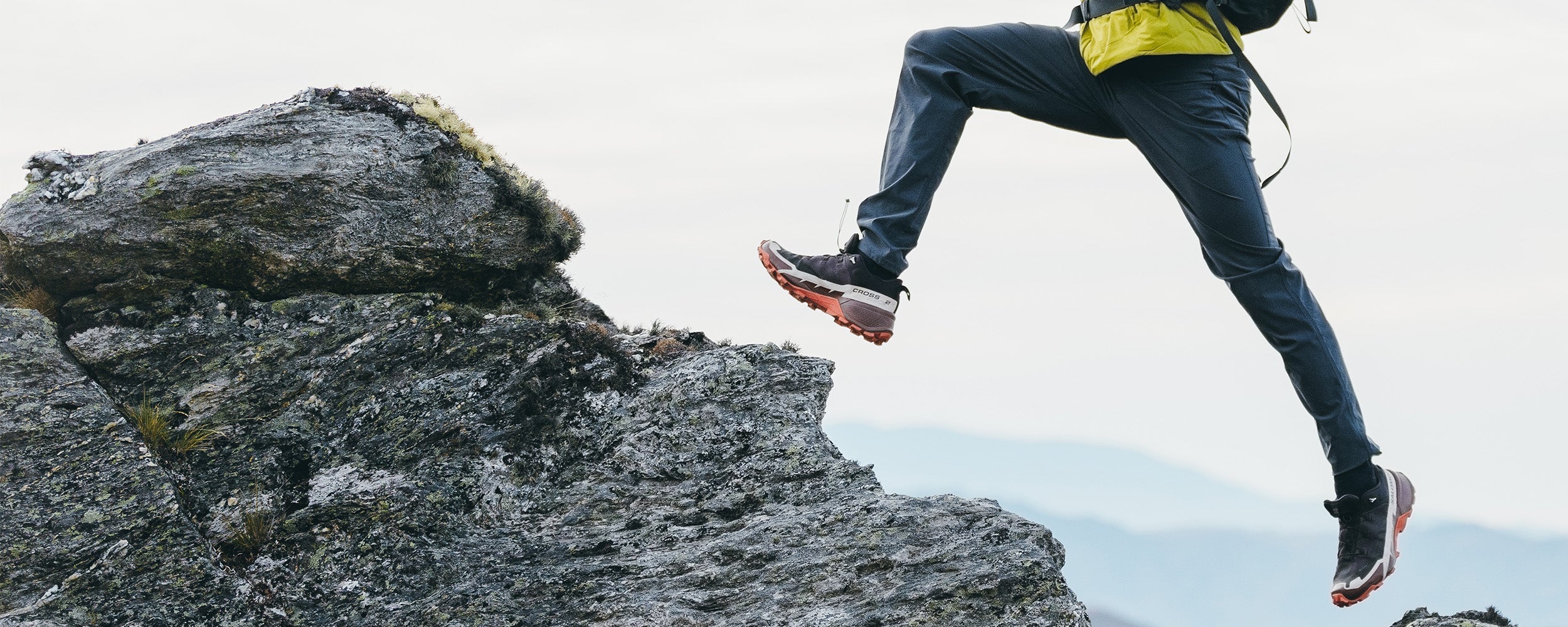 Male jumping across the rocks wearing Outdoor Research Men's Vesper Insulated Hoodie Rainforest and Ferrosi Pants in Naval Blue.