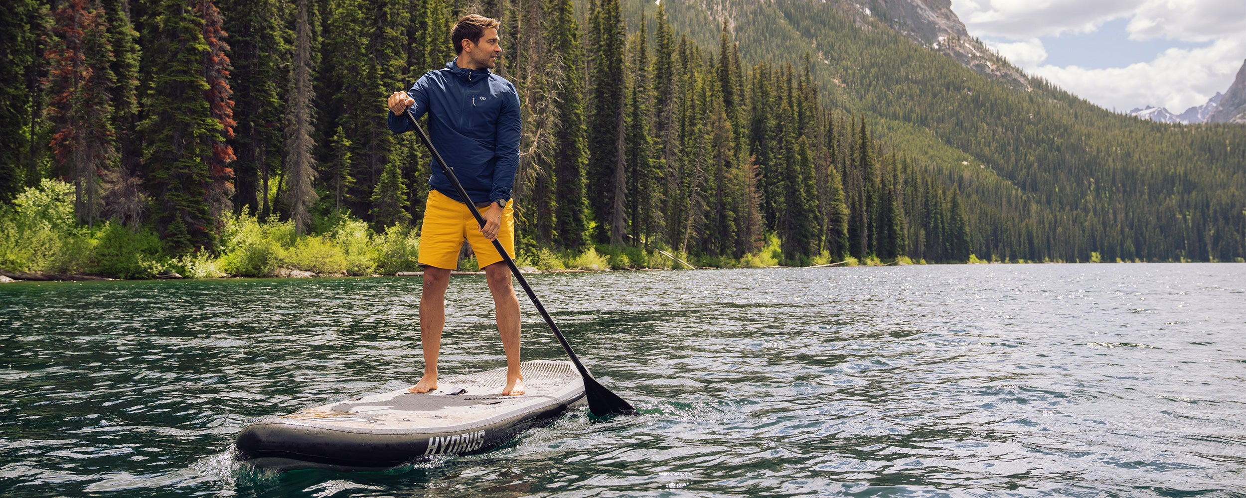 A man looks over his shoulder while stand up paddleboarding on a river in the mountains.