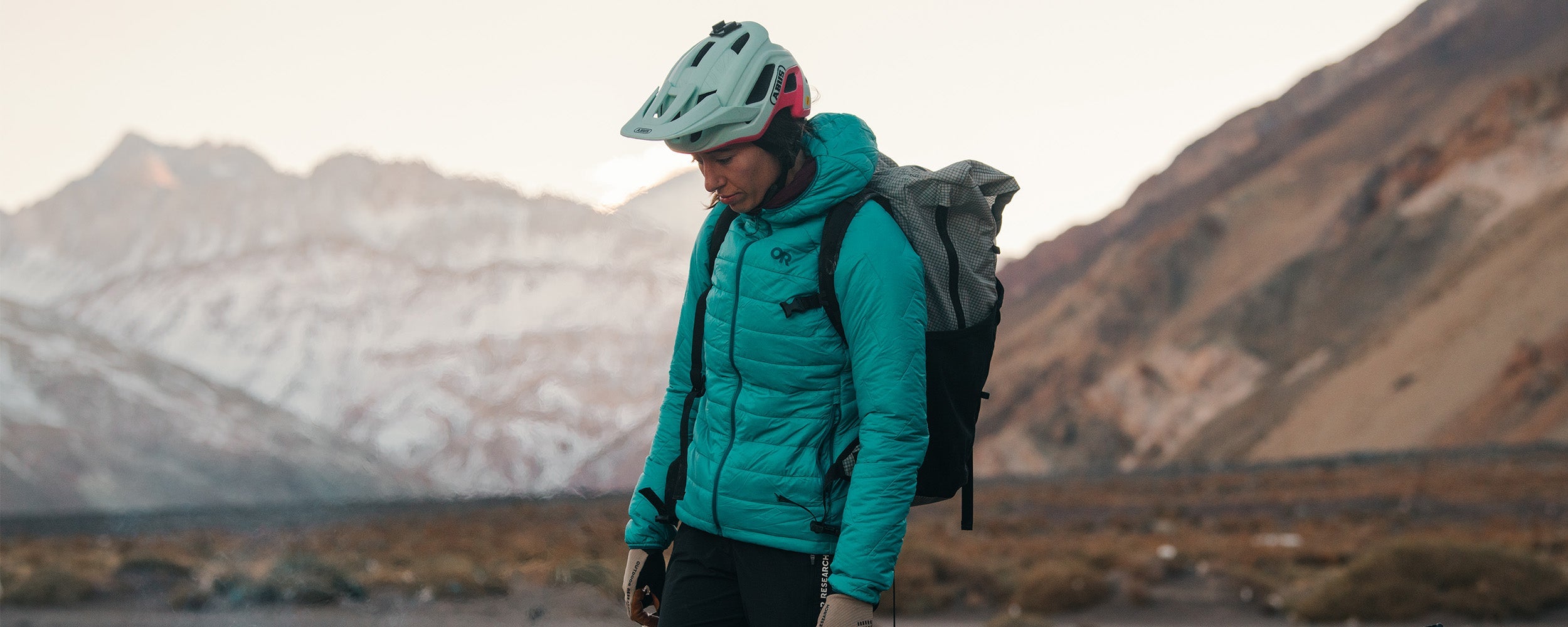 Female standing around campfire with bike gear on wearing Outdoor Research Women's Super Strand XT Hoodie Tidepool and Freewheel MTB Leather Palm Bike Gloves Pro Khaki. 