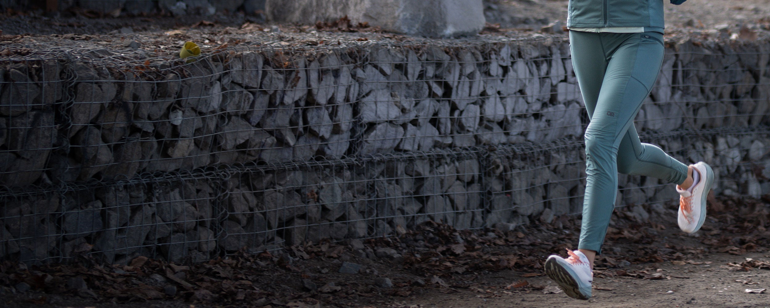 A woman runs along a path while wearing the Outdoor Research Deviator Wind Leggings.