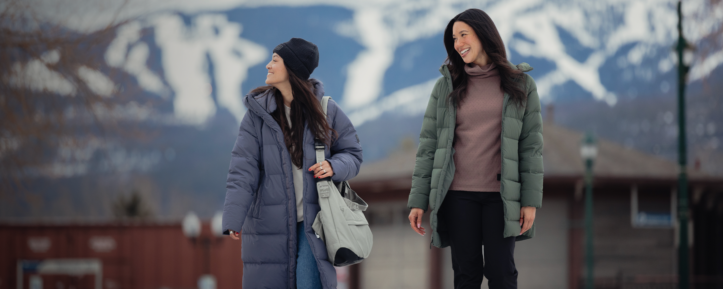 A woman stands by a wall wearing Outdoor Research Women's Coze Down Parka Atlantic and Women's Grayland Pullover Hoodie Summit. 