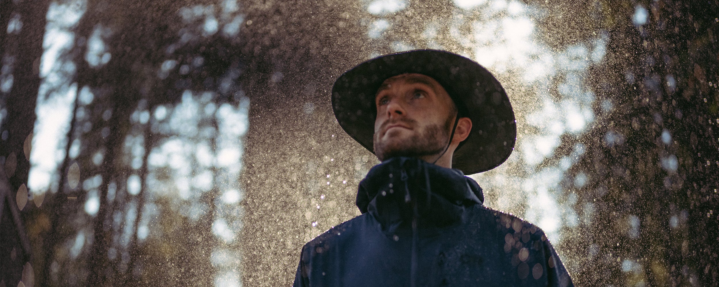 A man wears a rain hat on a rainy day in the woods.