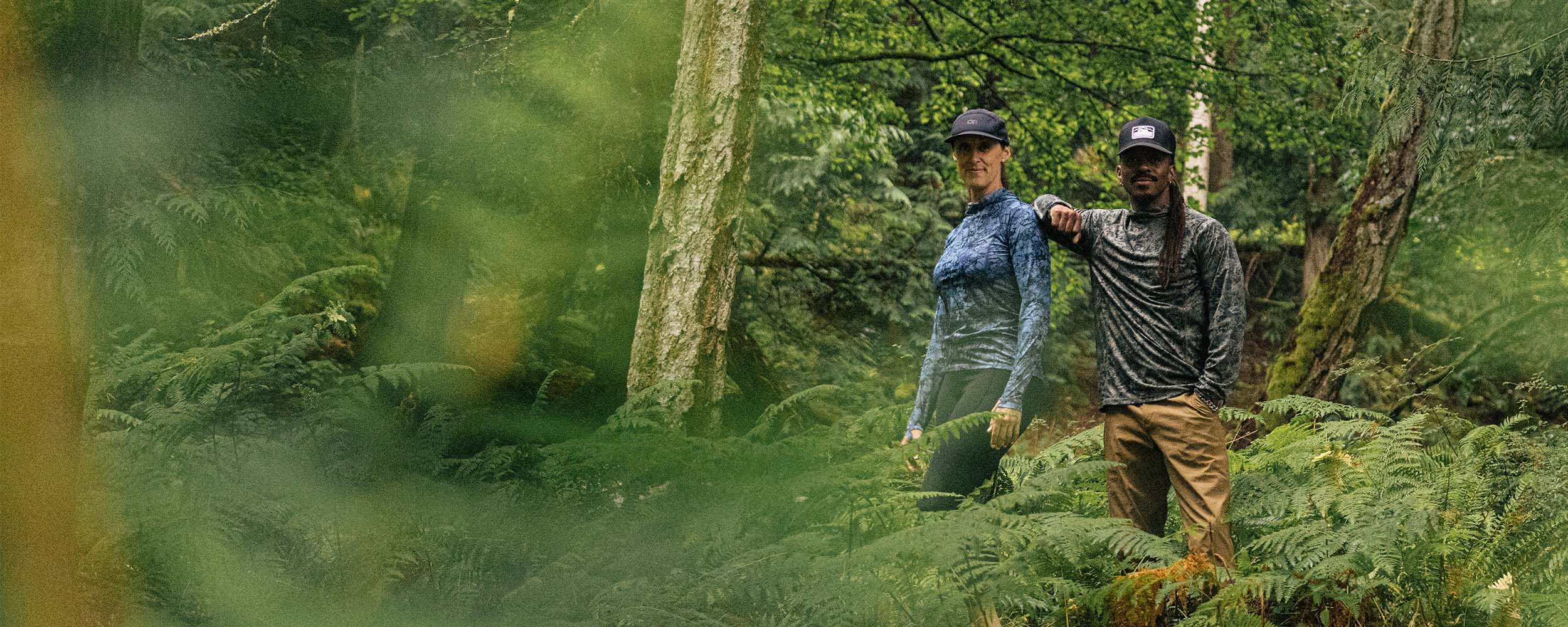 Two people hiking through a forest with greenery around them.