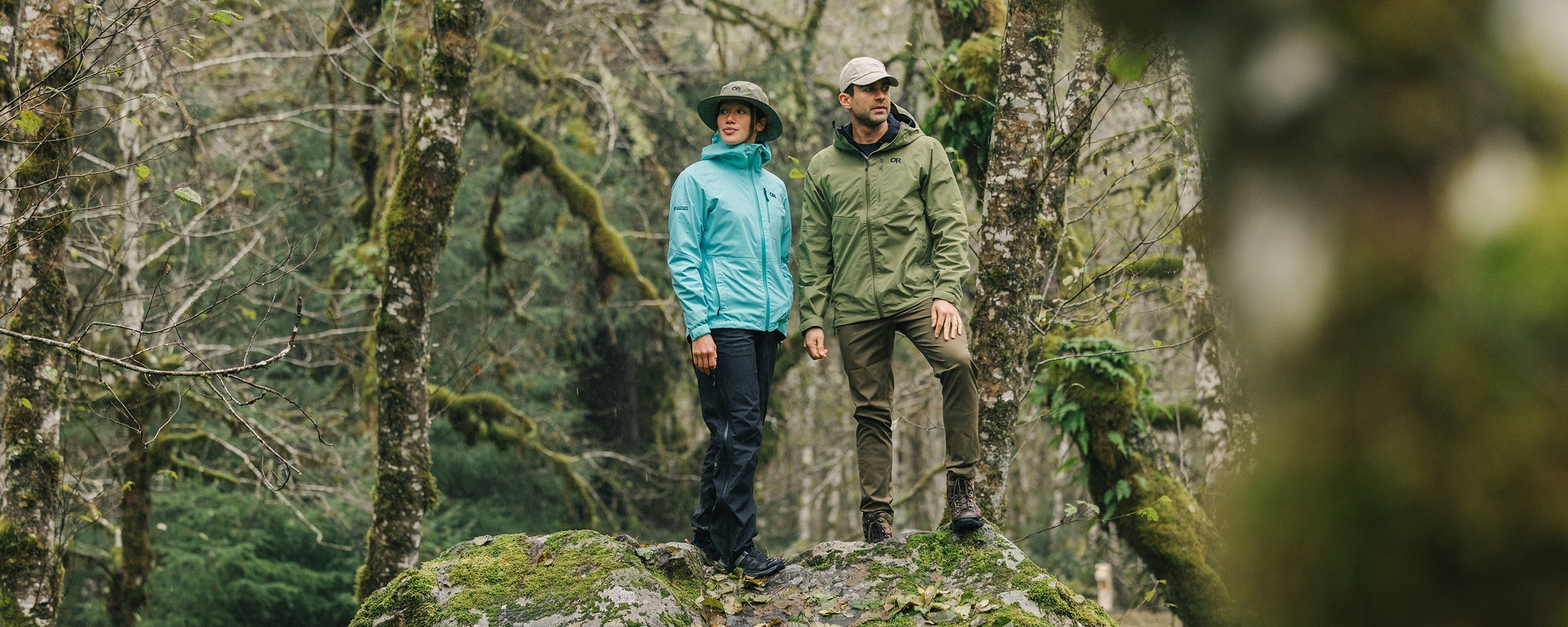 Two friends wearing Outdoor Research outerwear stand on top on a rock during a hike.