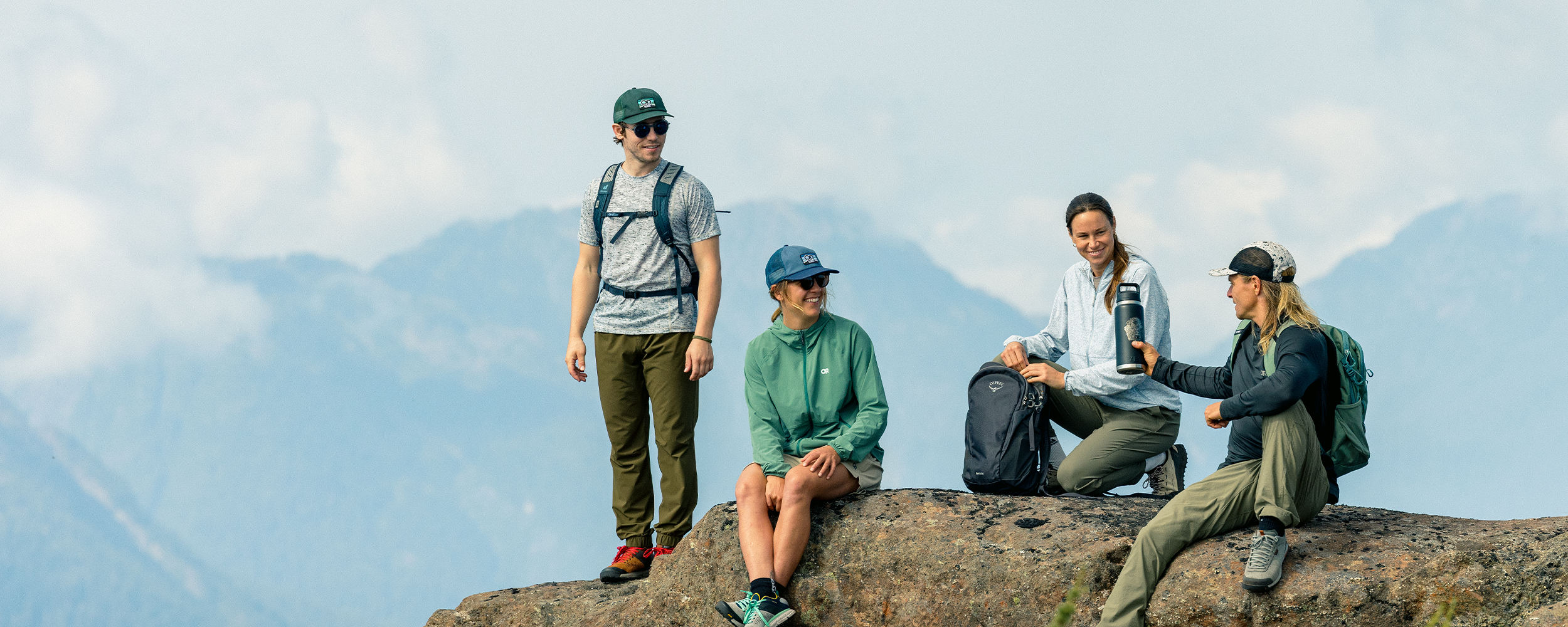 Four hikers resting at the top of the hill wearing Outdoor Research sportswear. 