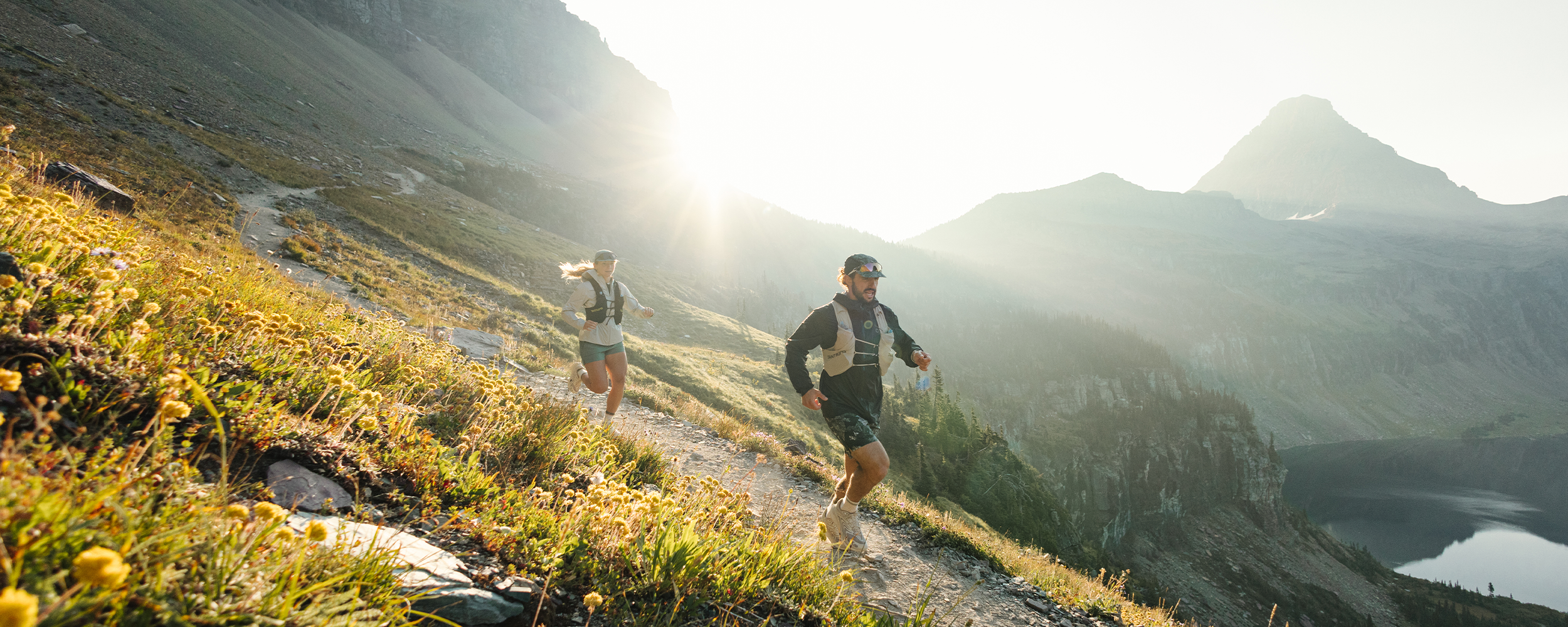 Two people trail running in the mountains with the sun behind wearing Outdoor Research sportswear. 