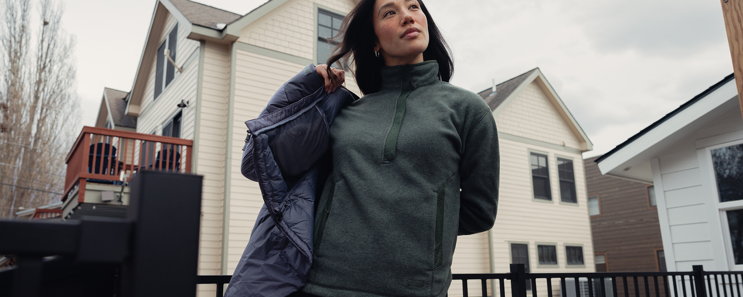 Woman putting on jacket wearing Outdoor Research Women's Deming Fleece Pullover Dark Laurel. 