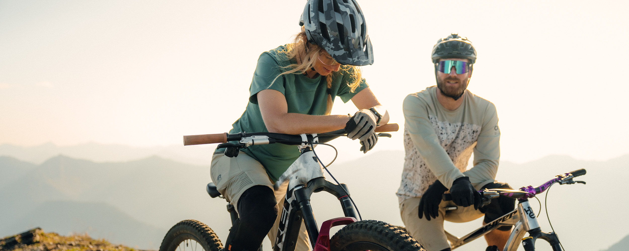 Two people on their bikes at the top of the mountain wearing Outdoor Research Freewheel MTB sportswear. 