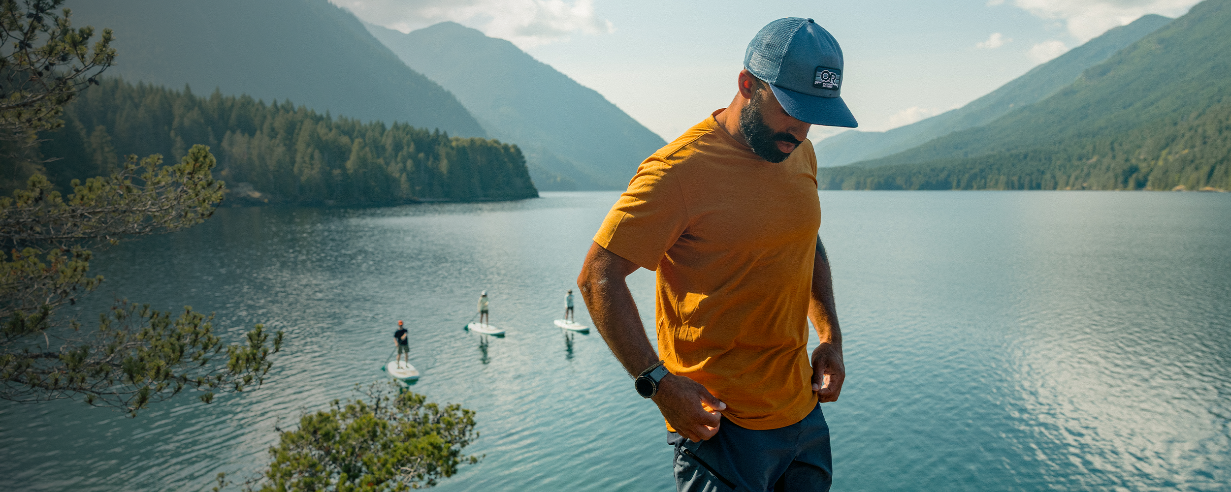 Three friends wearing Outdoor Research Sportswear rest on the side of a Float Plane beneath the sun.