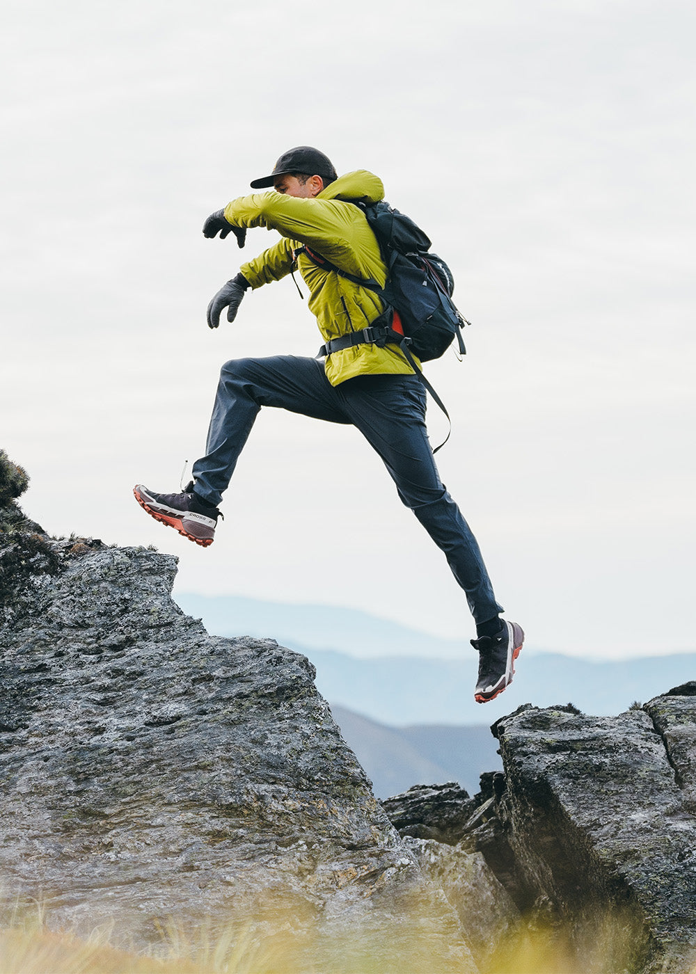 Male jumping across the rocks wearing Outdoor Research Men's Vesper Insulated Hoodie Rainforest and Ferrosi Pants in Naval Blue.