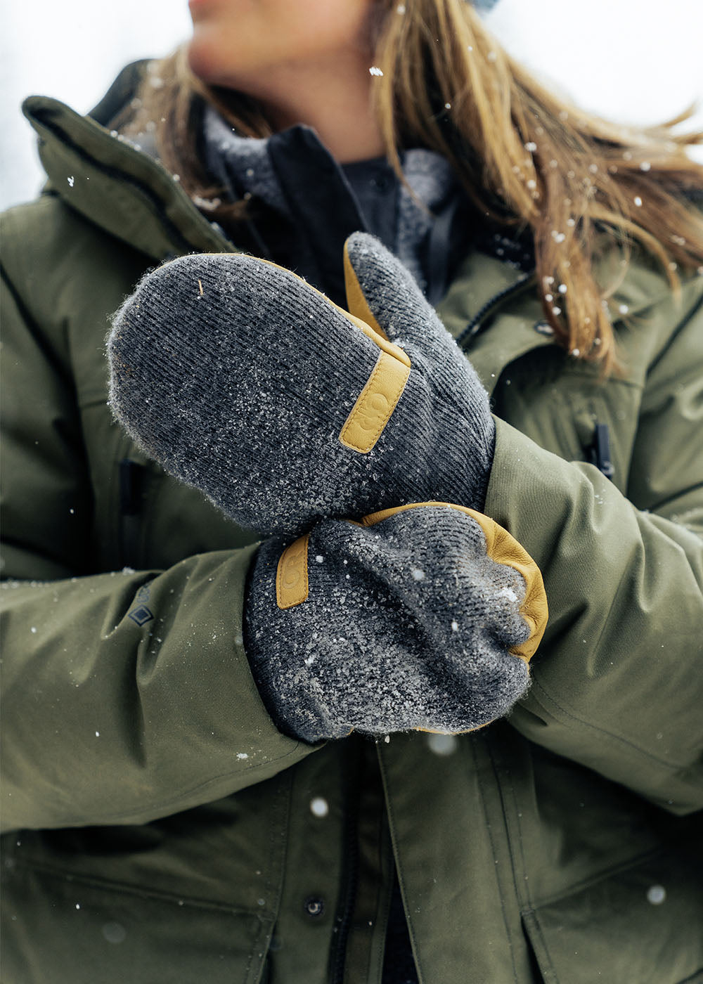 Zoe Atkin wears the Outdoor Research Coze Lux Down Parka in Ranger Green while carrying fire wood in the snow. 