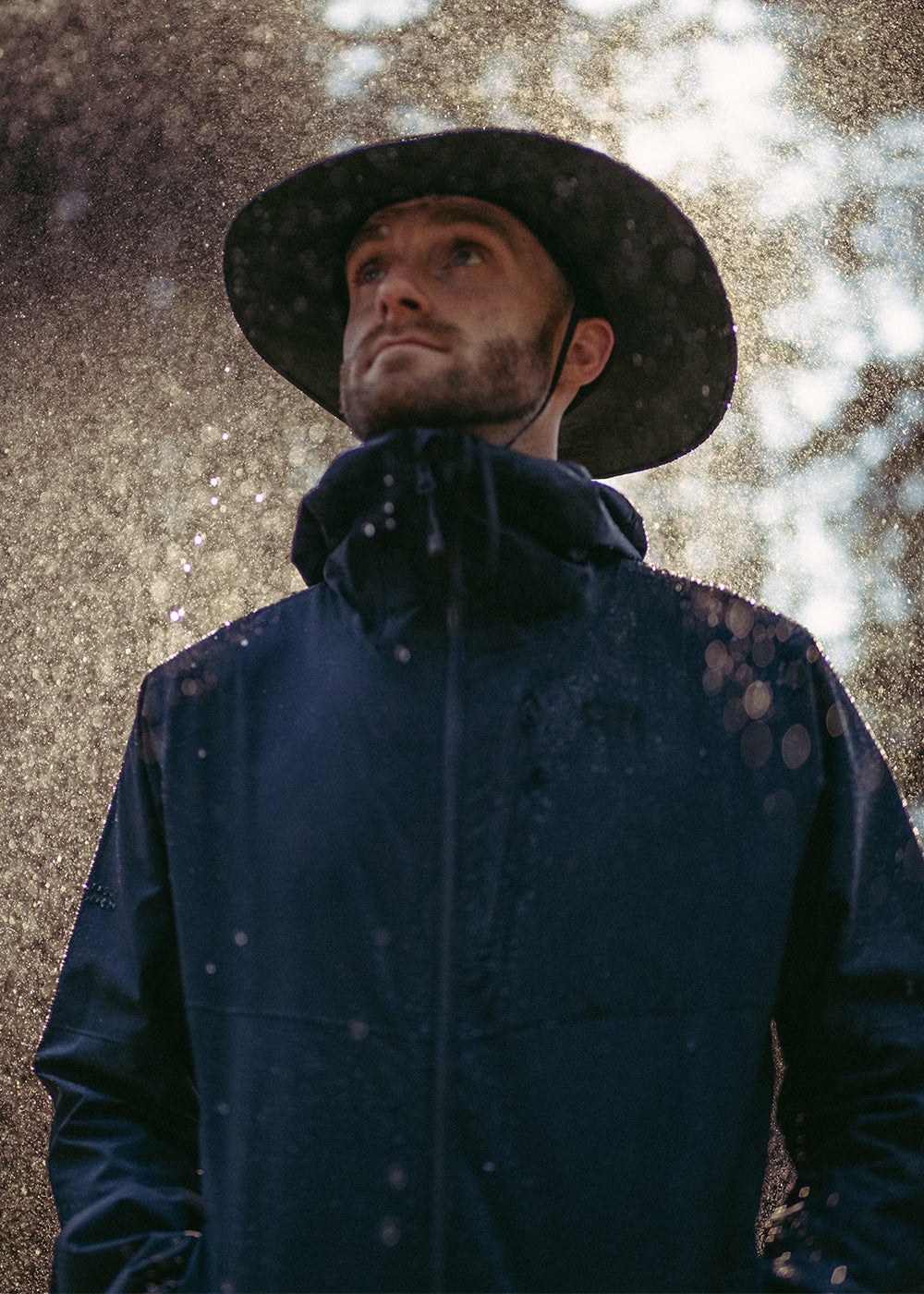 A man wears a rain hat on a rainy day in the woods.