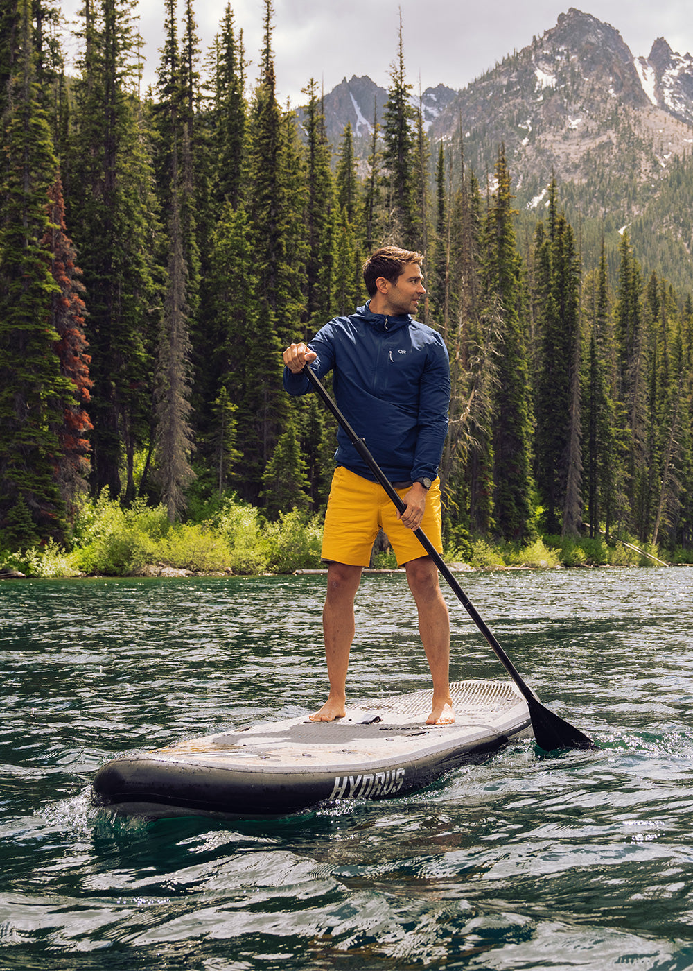 A man looks over his shoulder while stand up paddleboarding on a river in the mountains.