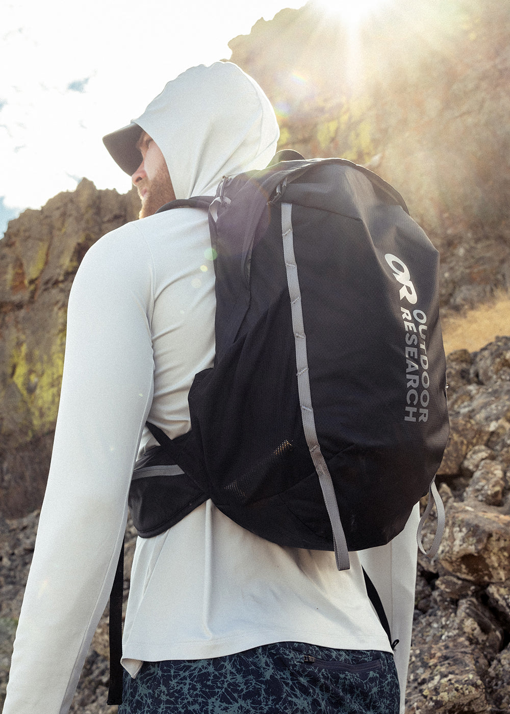 A man wears the Adrenaline Day Pack 30L in Black while hiking on a sunny day.