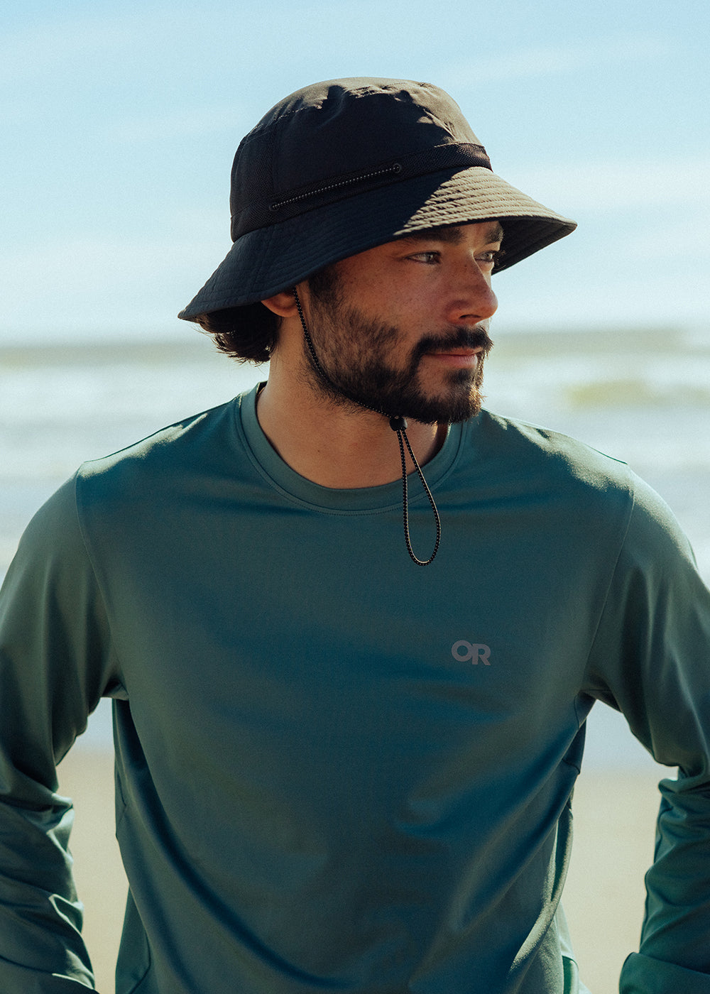 Man looks at the ocean view around him while wearing Outdoor Research ActiveIce Spectrum Sun Long Sleeve in Neptune.