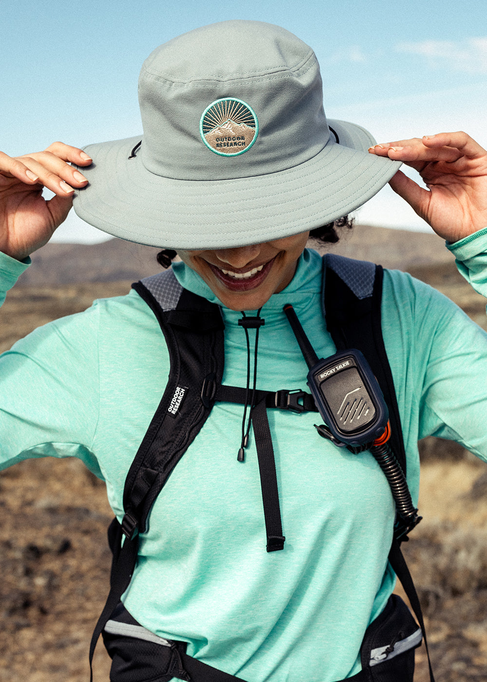 A woman smiles while grasping the sides of her Outdoor Research Heyday Boonie Hat in Neptune while out on a hike.