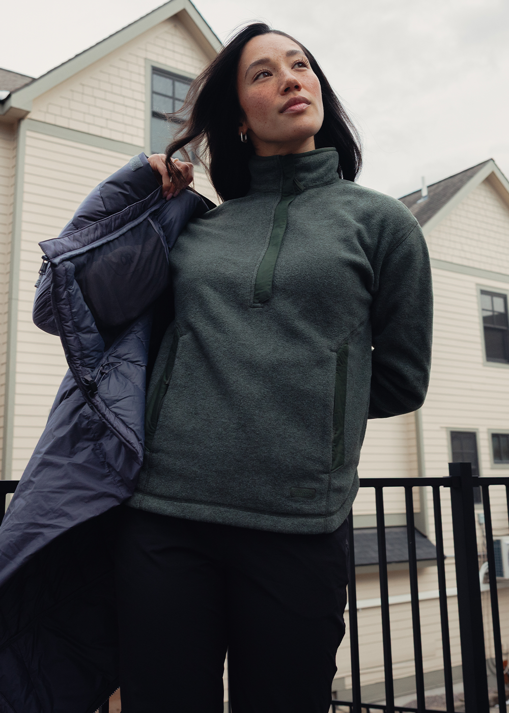 Woman putting on jacket wearing Outdoor Research Women's Deming Fleece Pullover Dark Laurel. 