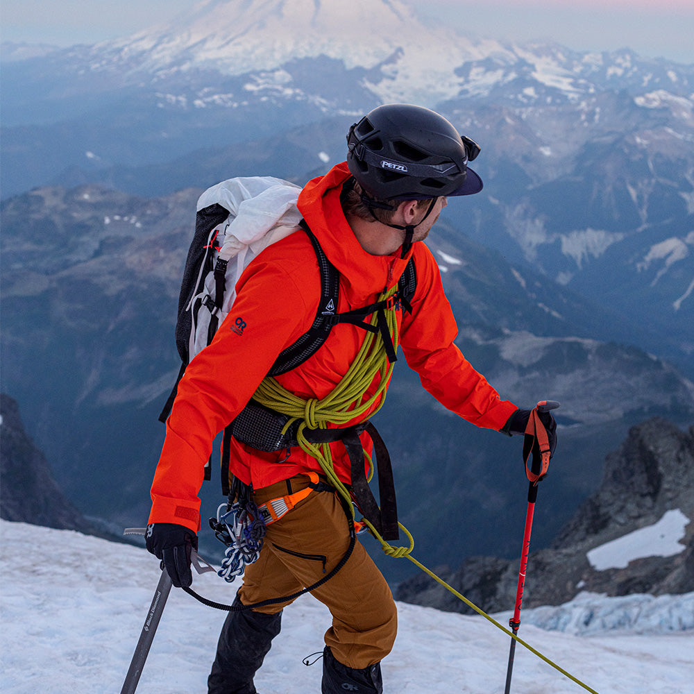 A mountaineer looks over their shoulder at the snow-covered mountain in the background.