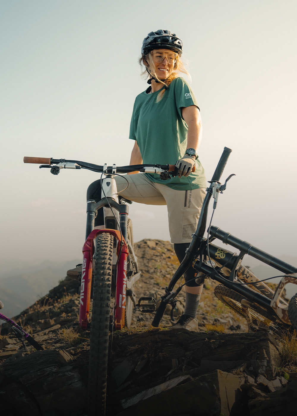 Female standing at the top of the hill with her bike wearing Outdoor Research Women's Freewheel MTB Ride Short and Women's Freewheel MTB Short Sleeve Jersey Malachite. 