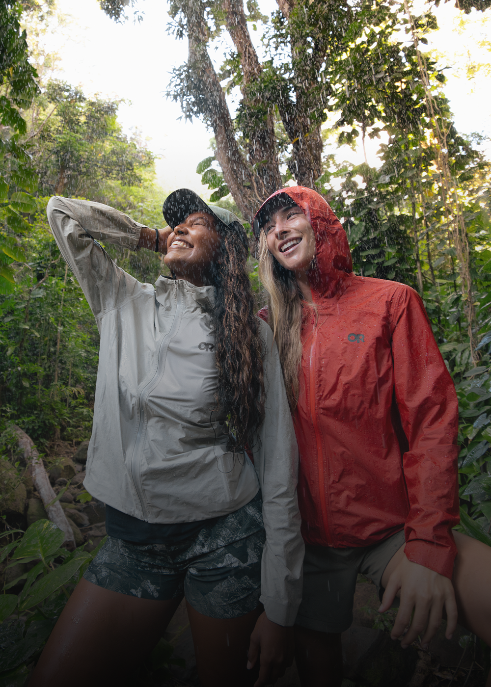 Two females in the rain wearing Outdoor Research Women's Helium UL Jackets Madrone Red and Oyster. 